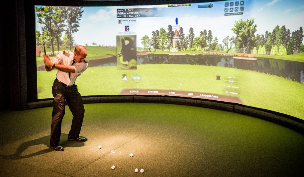 Airline pilot in the middle of golf swing in front of simulated screen in PGA airport lounge, MSP airport.