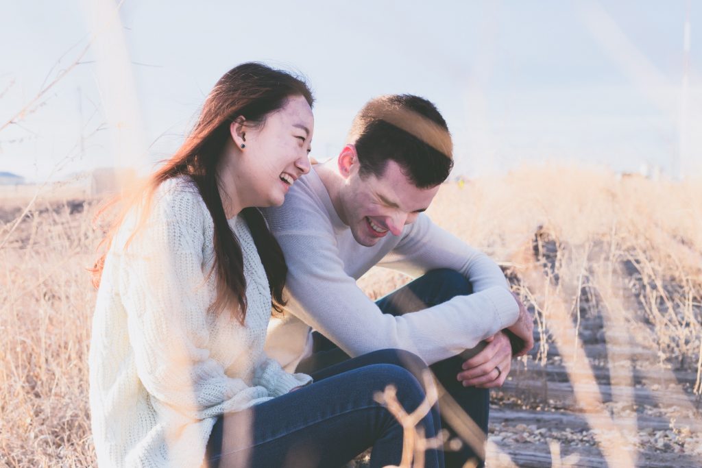 Couple laughing in field of grains on clear afternoon.