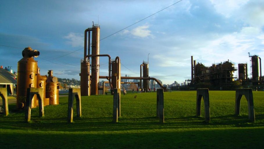 Large industrial gas pipelines surrounded by greenery and grey-blue sky. 