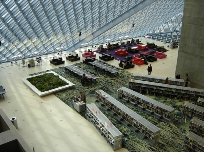 The main floor lobby of the grand Seattle library, with vegetation and giant slanted glass wall.