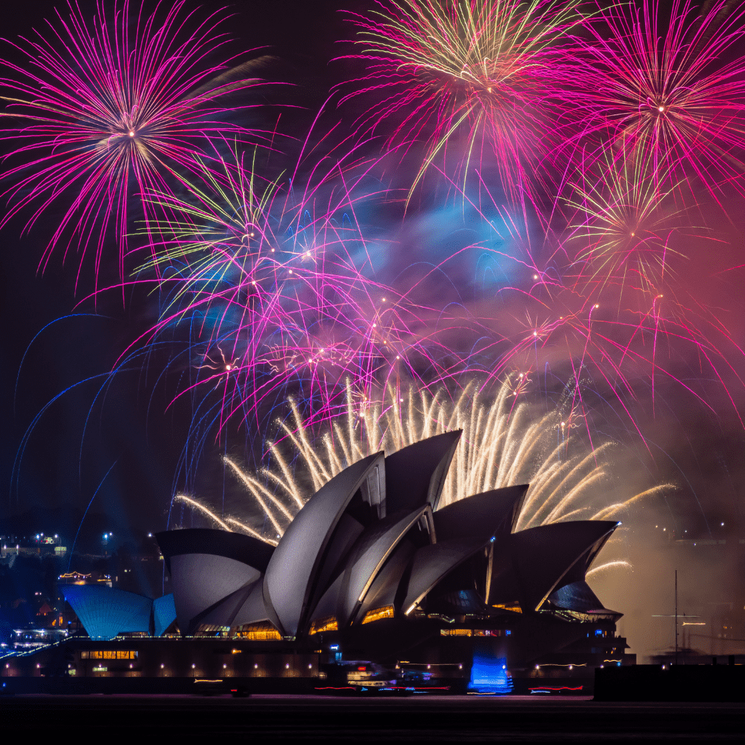 Vibrant fireworks burst above Sydney Opera House, celebrating New Year's Eve against the night sky.