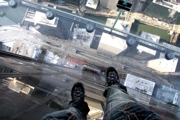 Waist-down view from Willis Tower sky deck looking straight over other Chicago high rises.