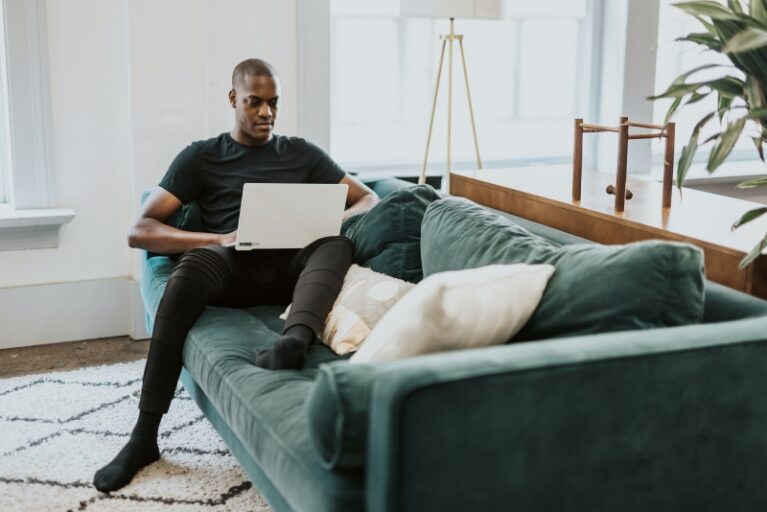 working from home, with laptop on couch with blanket and pillow.