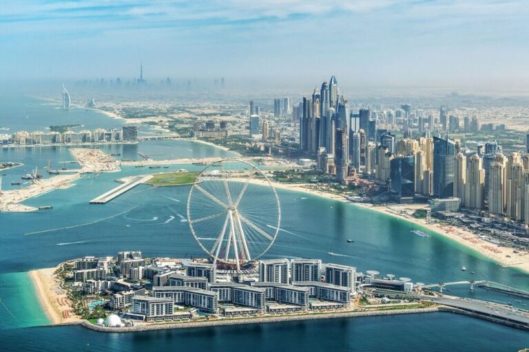 Aerial view of Dubai's coastline with skyscrapers and a giant Ferris wheel.