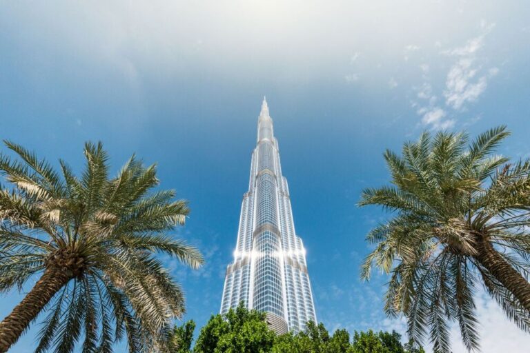 The Burj Khalifa towers over palm trees against a clear blue sky.
