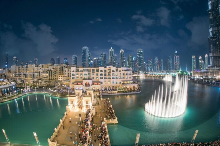 Dubai Fountain show with bustling crowd and lit city skyline.