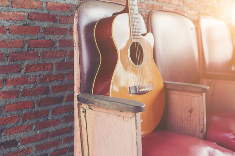 enjoy nashville in one day: a guitar sitting upright in an auditorium chair against a brick wall background