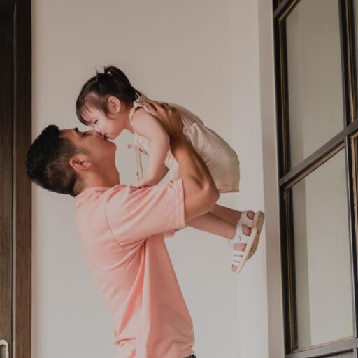 father kissing daughter as he picks her high up into the air.