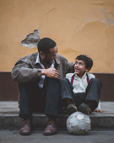 father and son enjoying time together sitting on the sidewalk with soccer ball in Mexico.