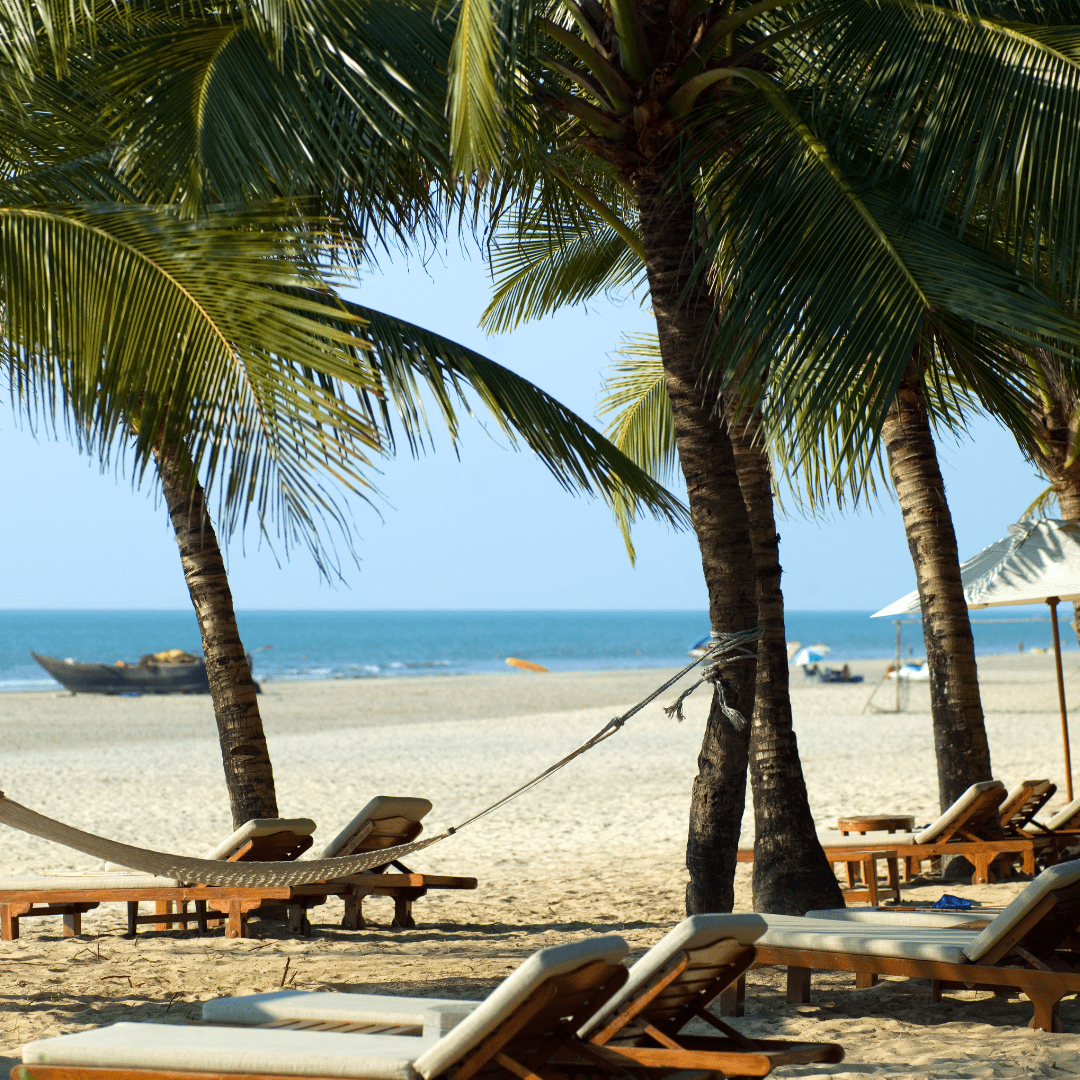 Sunny Goa beach with palm trees, lounge chairs, and a boat on the tranquil sea.