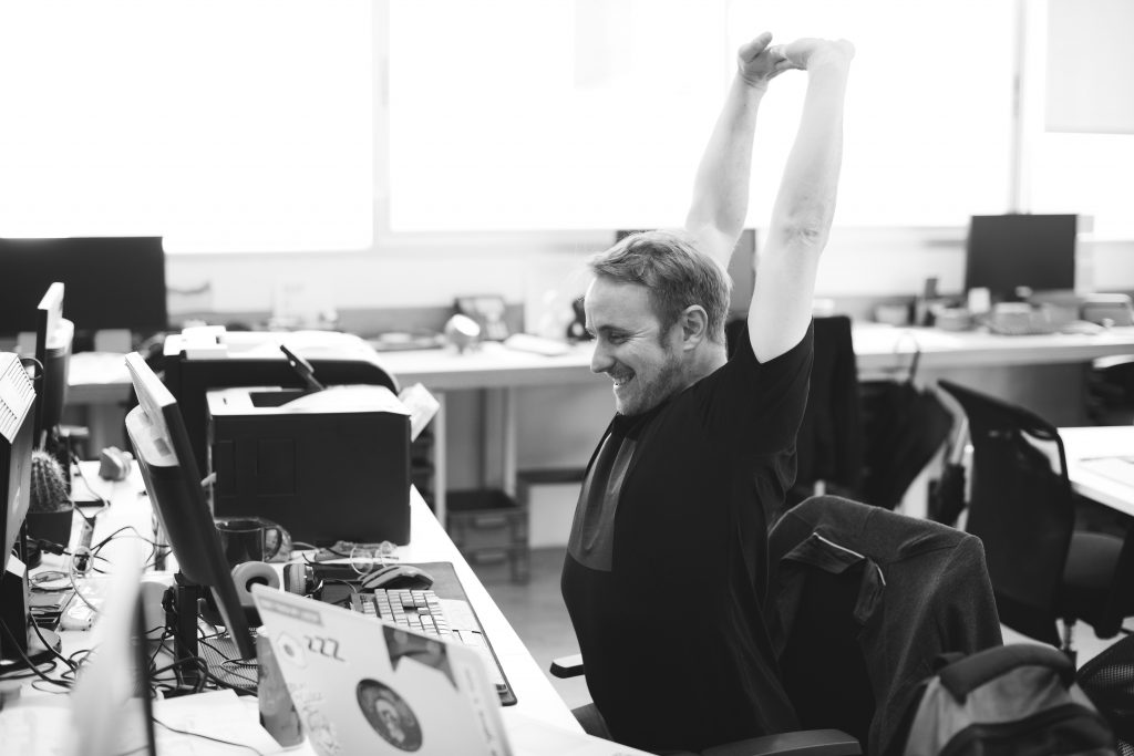 Office worker stretches his arms high and smiles after being productive and earning himself a much-deserved break. 
