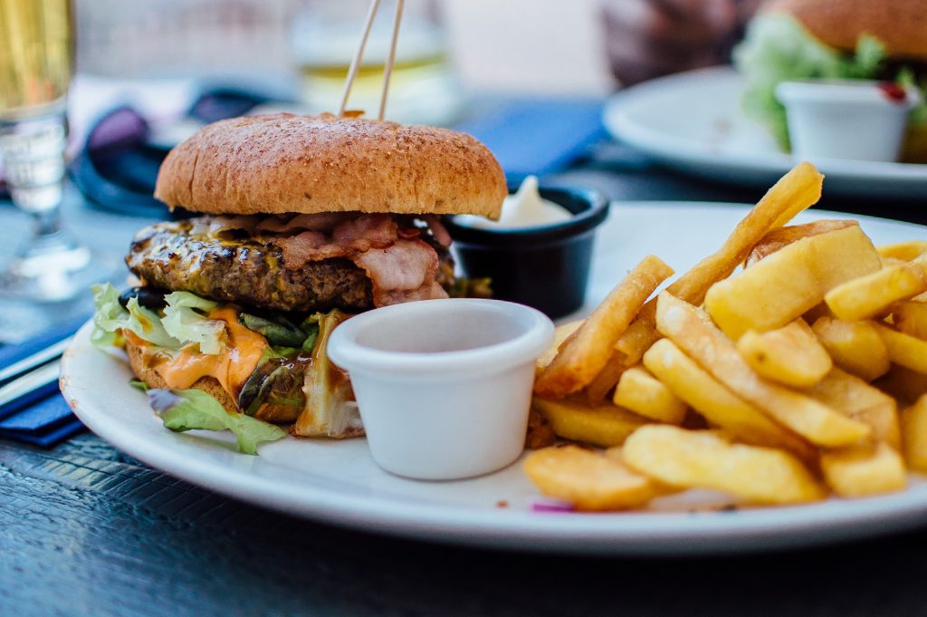 Juicy burger with fries, mayonnaise and ketchup on white plate.