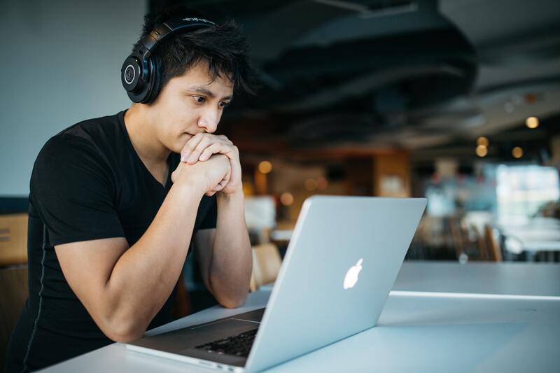 Man reads on laptop with headphones on at cafe. 