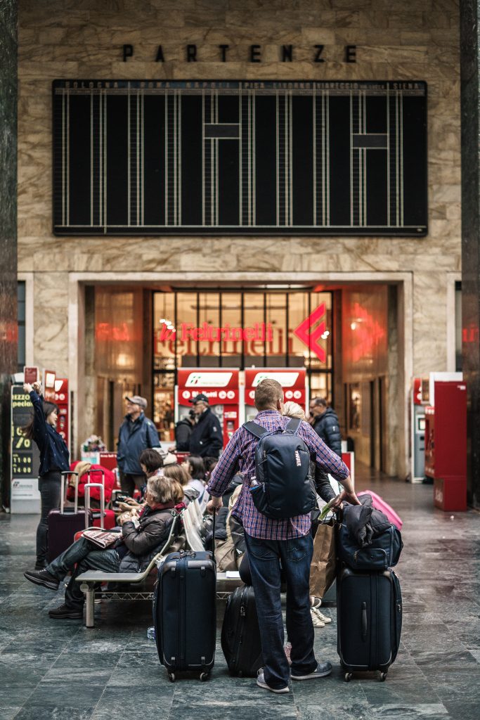 Man stands with various luggage in city center.